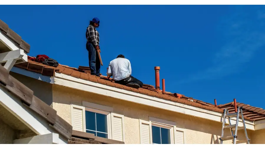 Roof construction scene with workers on a tiled roof, captured under a clear blue sky.