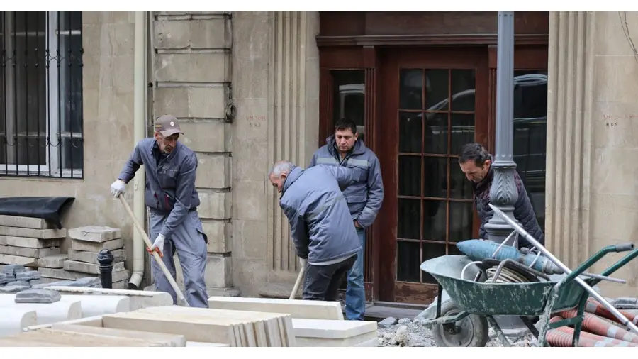 Team of men working on paving new city sidewalk with stones. Urban construction scene with workers.