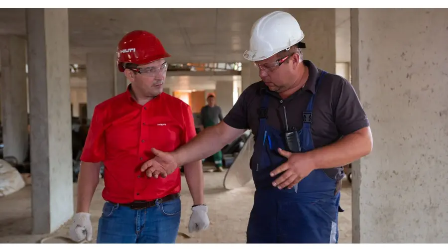 Two construction workers in safety gear discussing plans at a construction site.