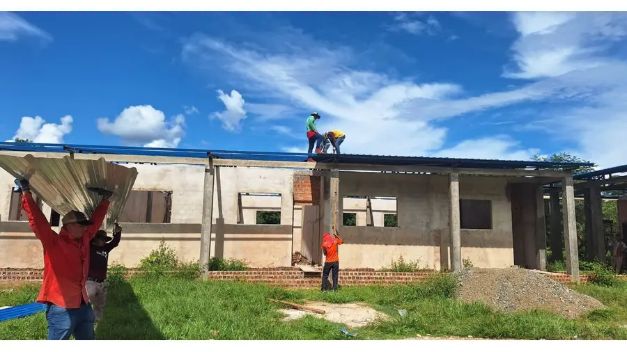 Workers install roofing on an unfinished building under a bright blue sky.